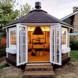 Беседка барбекю восьмигранная с распашными дверями и теплым светом внутри на участке в Подмосковье